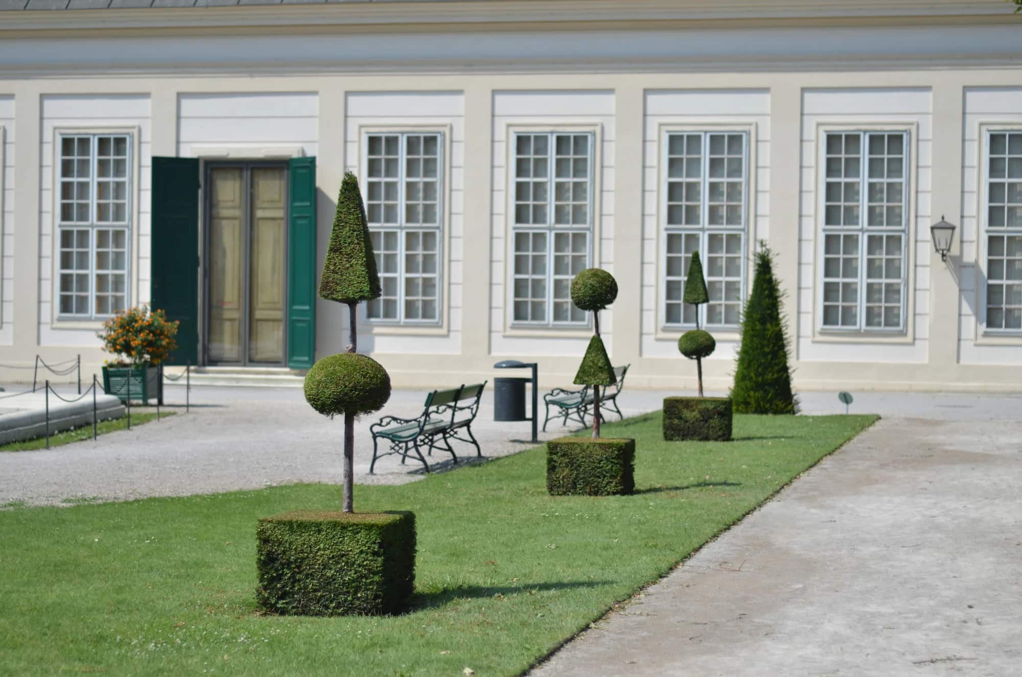 Façade claire d’une maison de caractère, devant sa pelouse et ses arbres taillés