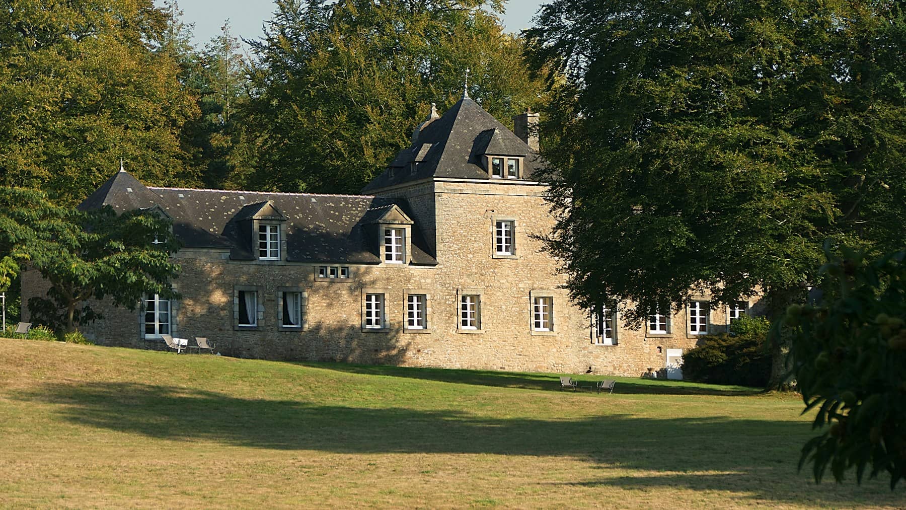 Maison de maître en pierre aux toits d’ardoise, entourée d’un parc