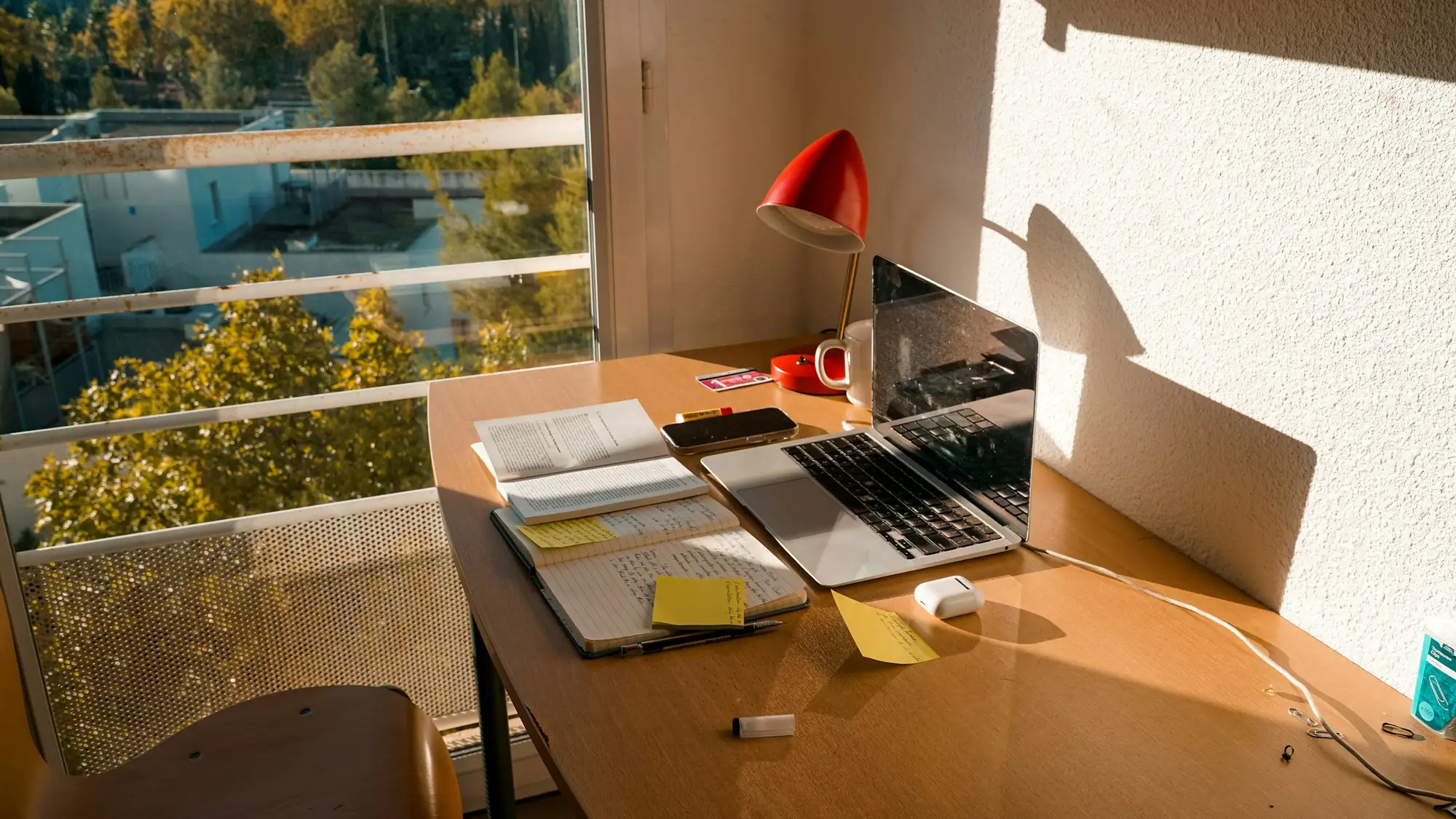 Table de travail claire près d’une grande fenêtre, ordinateur portable et dossiers ouverts