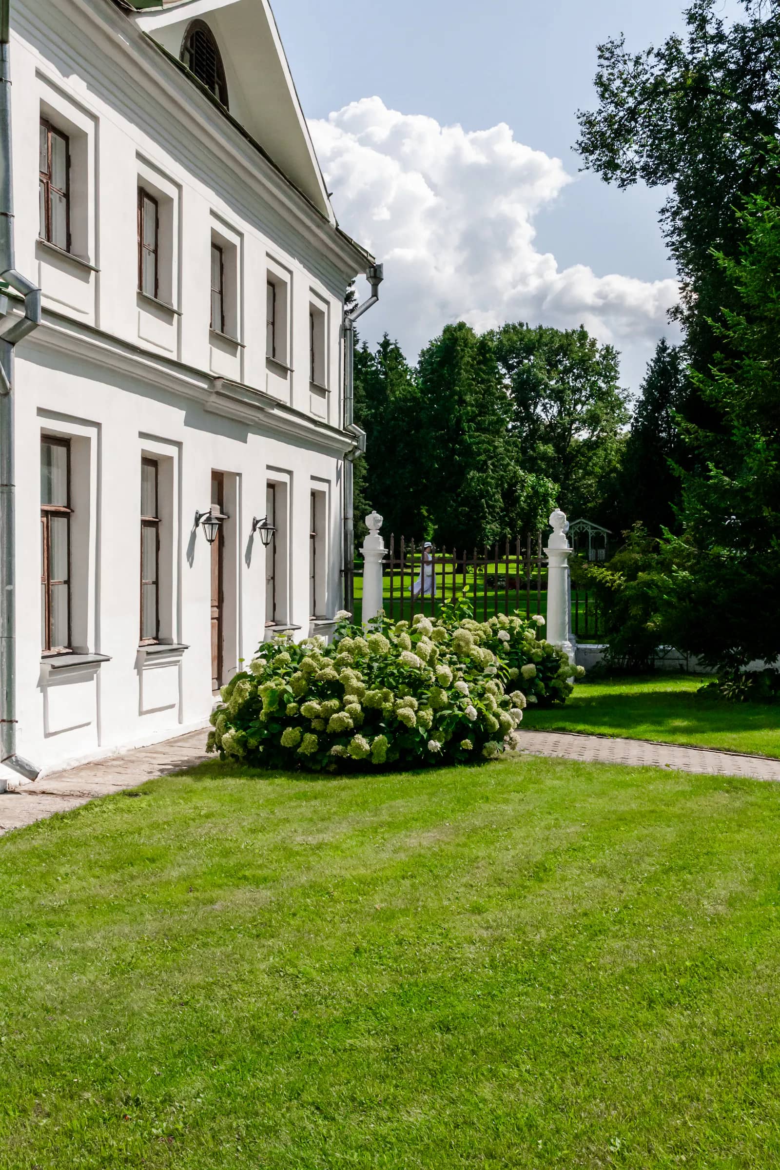 Grand jardin tondu devant une maison de caractère au crépi clair, bordé de massifs