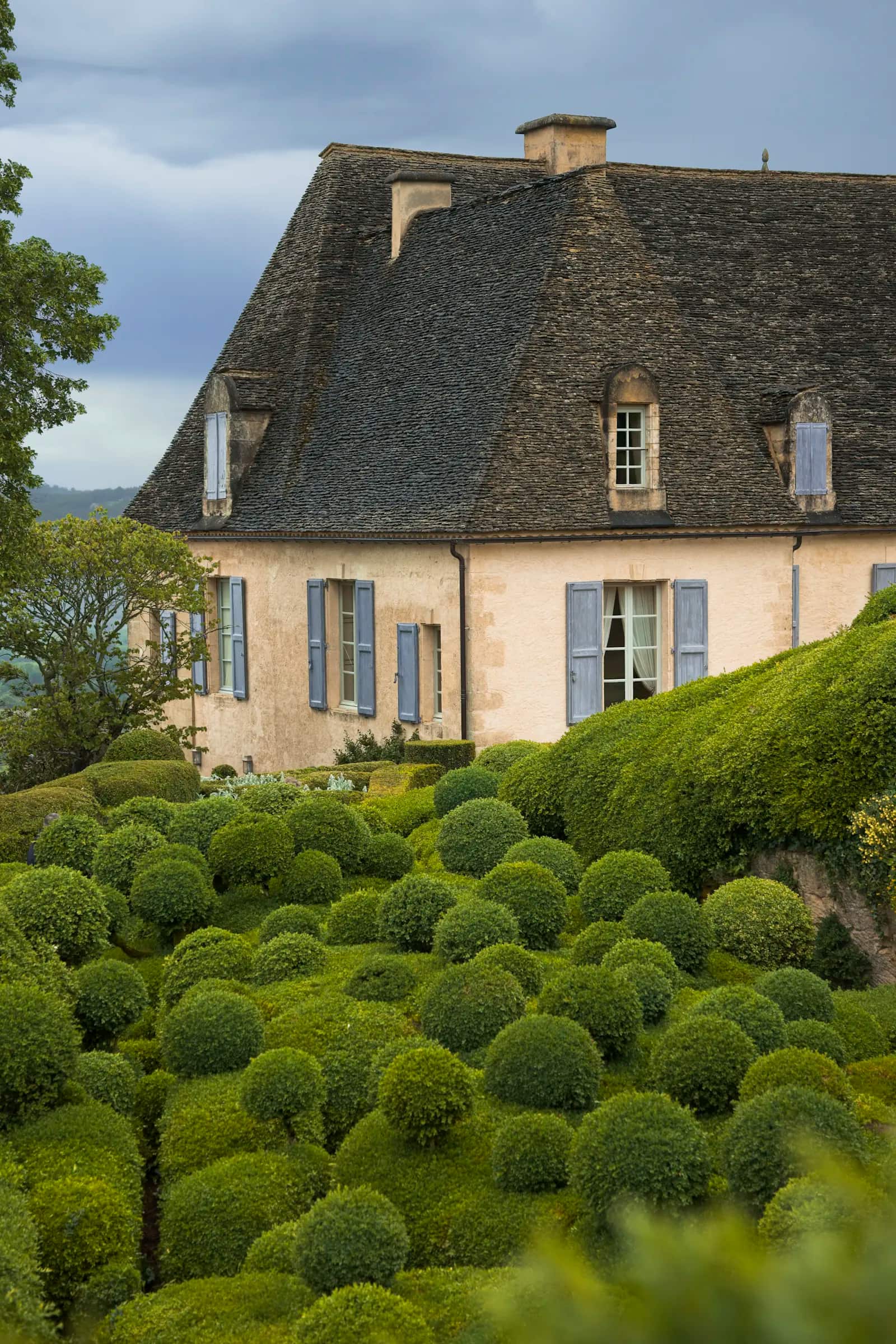 Maison de caractère au crépi clair et au toit de tuiles, devant son jardin aux buis taillés