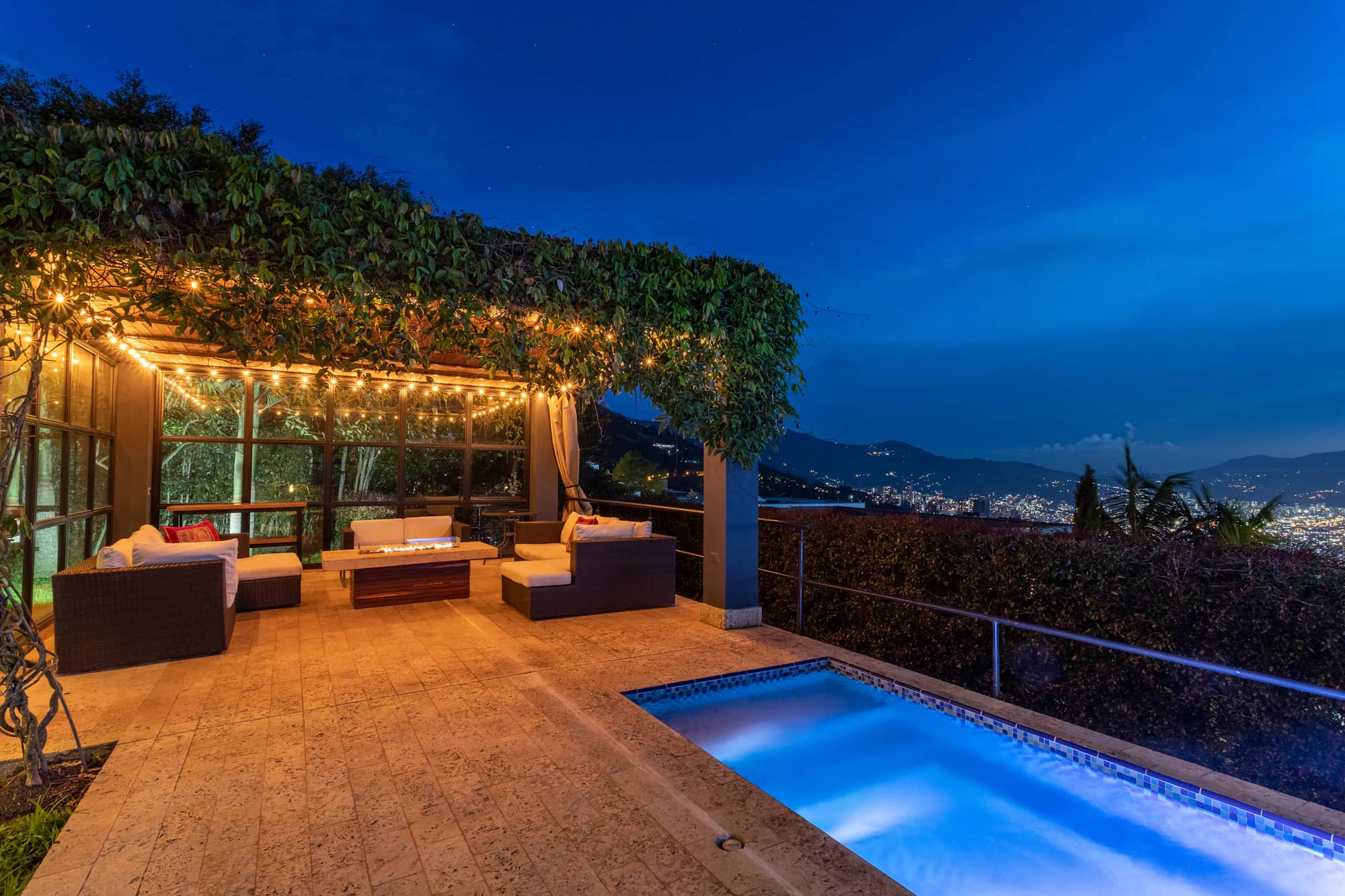 Terrasse d’une villa au bord de sa piscine, pergola de bois éclairée en fin de journée